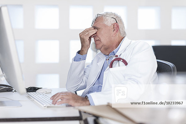 Overworked senior doctor sitting at desk working on computer
