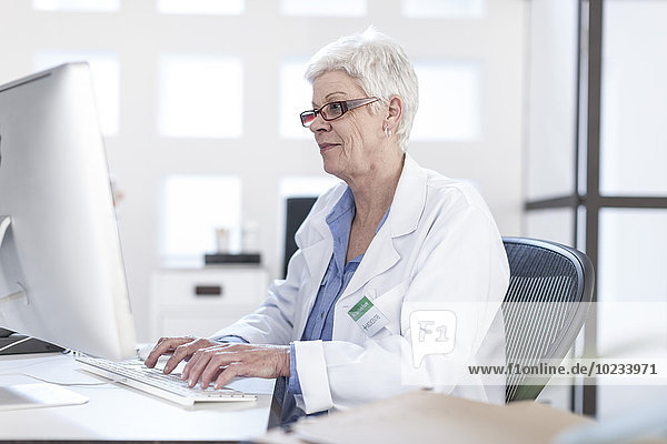 Senior woman in lab coat working on computer