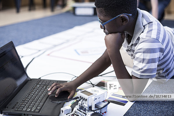 Schuljunge mit Laptop im Robotikklassen-Testfahrzeug auf der Teststrecke
