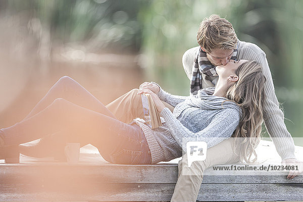 Junges Paar,  das sich auf einem Steg am See küsst
