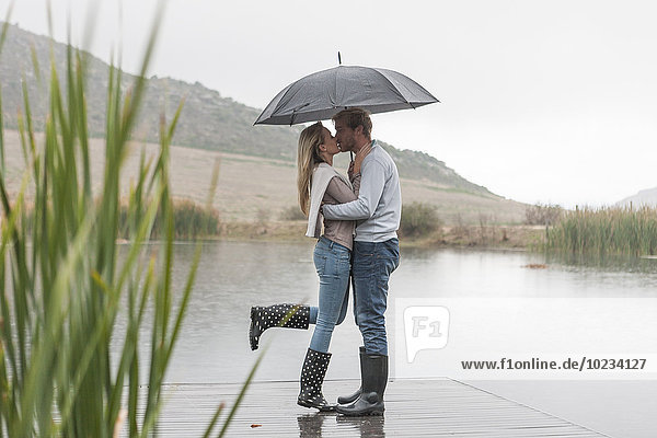 Kissing couple standing in the rain with umbrella