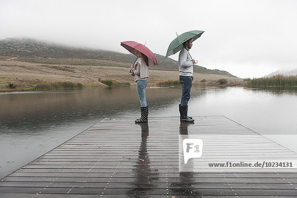 Paar im Regen stehend auf Holzsteg mit Regenschirmen