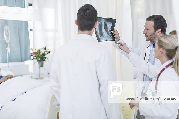 Drei Ärzte sehen sich das Röntgenbild in einem Krankenhauszimmer an.