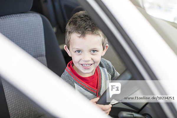 Happy boy at car dealer inside car steering