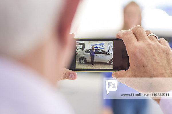 Man taking picture of woman at a new car in showroom