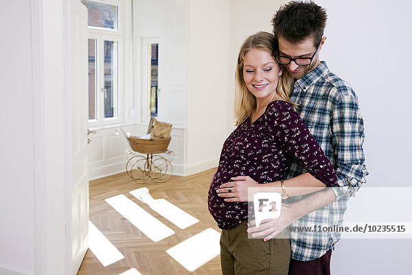 Young man embracing pregnant woman in new home with pram in background