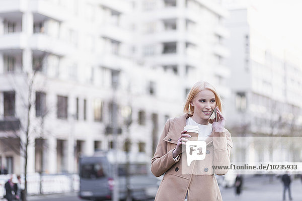 Deutschland  Berlin  junge Frau mit Kaffee zum Telefonieren mit Smartphone