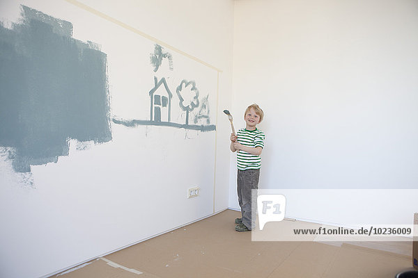 Kleiner Junge malt Haus und Baum an der Wand seines neuen Zimmers