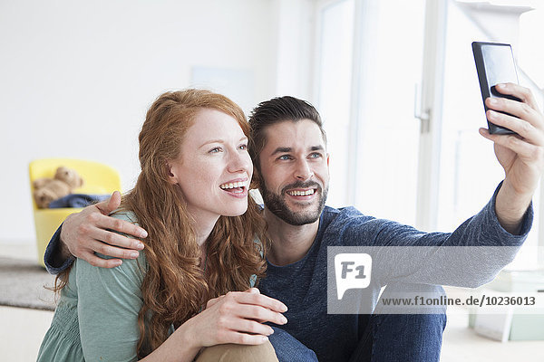 Lächelndes junges Paar  das einen Selfie mit Smartphone im Wohnzimmer nimmt.
