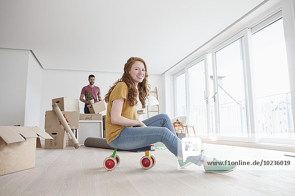 Young couple moving into new flat  woman sitting on toy cart