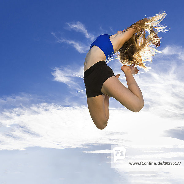 Junger Sportler beim Springen unter blauem Himmel