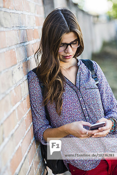 Brunette young woman with glasses looking at cell phone