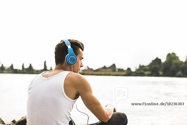 Young man by the riverside wearing headphones