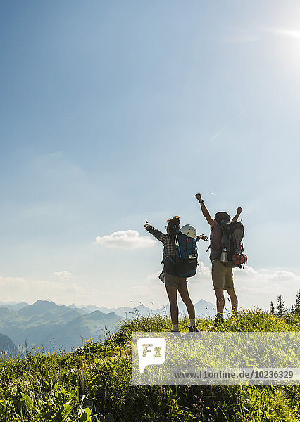 Österreich  Tirol  Tannheimer Tal  jubelndes junges Paar auf dem Bergweg stehend mit Blick auf die Aussicht