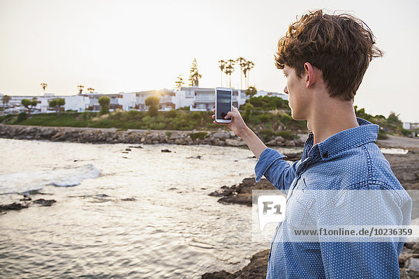 Griechenland  Rhodos  junger Mann fotografiert mit Smartphone am Meer