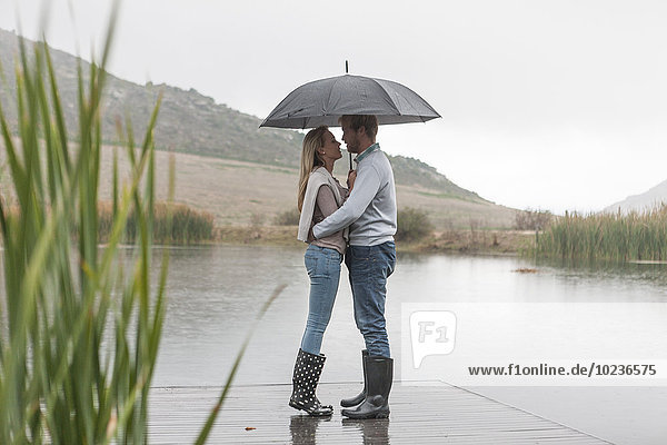 Paar im Regen stehend auf Holzsteg mit Schirm