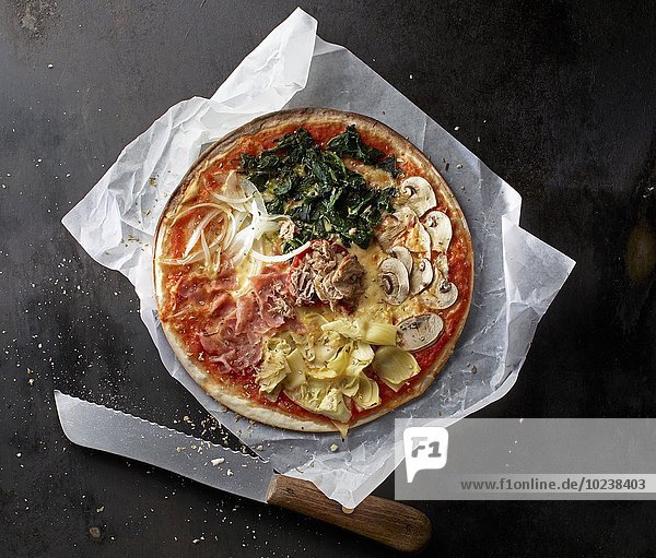 Pizza mit Spinat  Champignons  Artischocken  Parmaschinken  Zwiebeln und Thunfisch auf Papier mit Messer