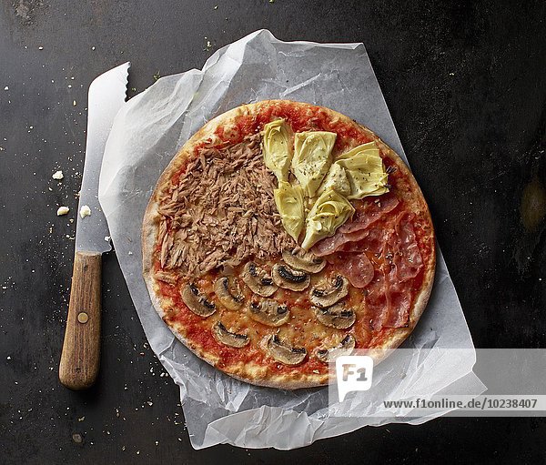 Pizza mit Thunfisch  Champignons  Parmaschinken und Artischocken auf Papier mit Messer