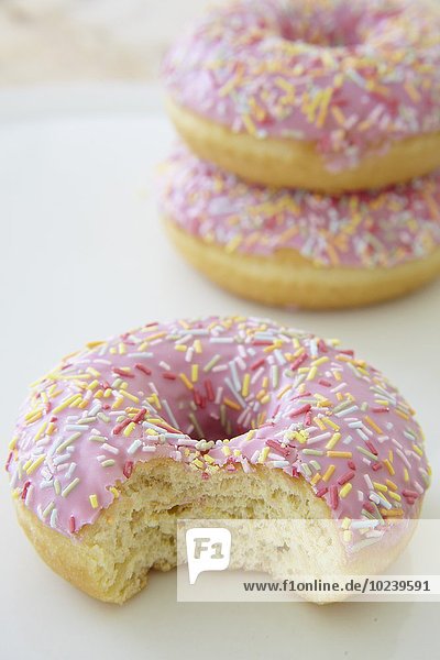 Pinkfarbene Doughnuts mit Zuckerstreuseln  eins angebissen
