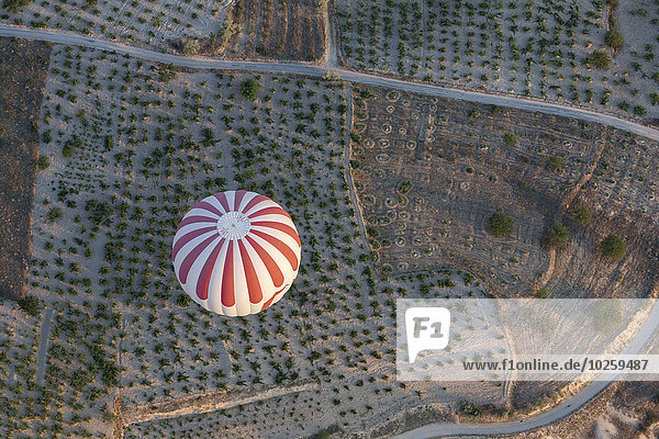 Hochwinkelansicht eines gestreiften Heißluftballons über der Agrarlandschaft