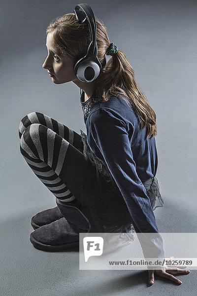 Durchgehende Seitenansicht des Mädchens beim Musikhören über Kopfhörer über grauem Hintergrund