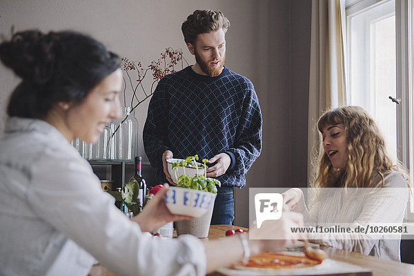 Young man with female friends making pizza at table