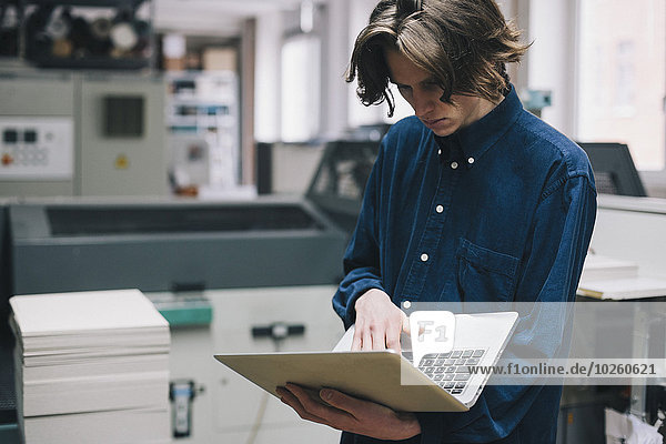 Junger Techniker mit Laptop in der Fabrik