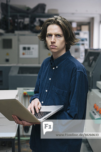 Porträt eines selbstbewussten jungen Technikers mit Laptop in der Fabrik