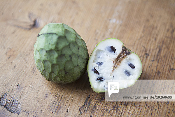 High angle view of whole and halved cherimoya on wooden table