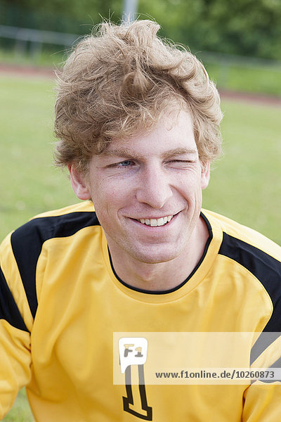 Happy young soccer player sitting on field