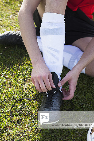 Low section of man tying soccer shoe on field