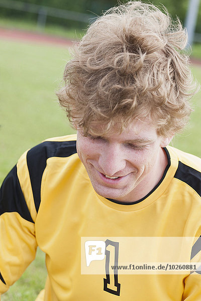 Happy young soccer player sitting on field