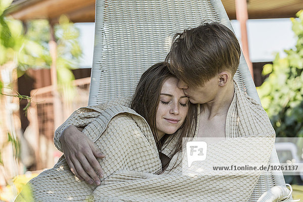 Romantic young couple wrapped in blanket on hanging chair outdoors