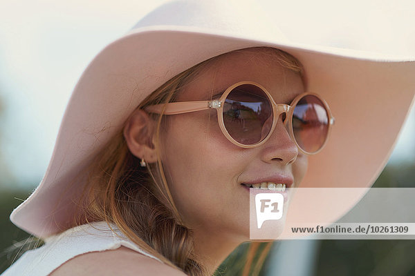 Porträt einer jungen Frau mit Sonnenbrille und Hut im Park