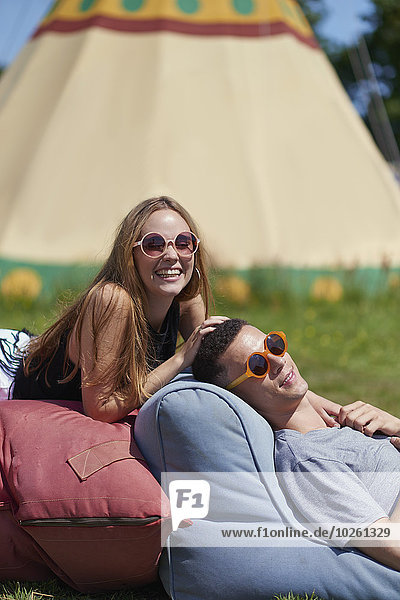 Happy couple lying on pillows while glamping  teepee in background