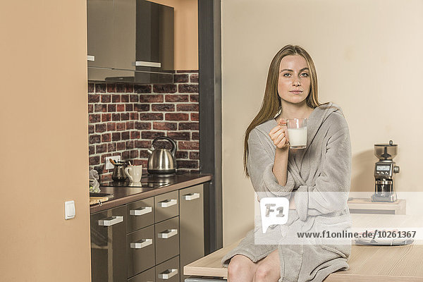 Porträt einer selbstbewussten jungen Frau im Bademantel  die zu Hause Milch im Becher trinkt.