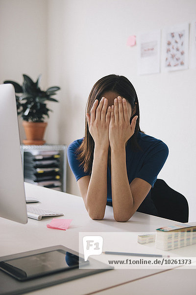 Müde Geschäftsfrau bedeckt Gesicht mit Händen am Schreibtisch
