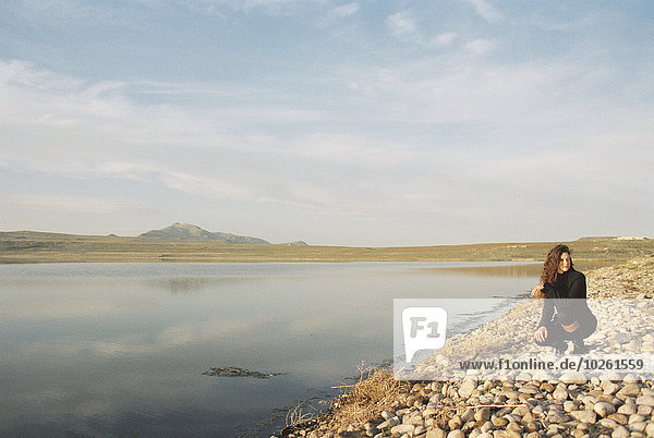 A woman collecting pebbles on the shore of a lake.