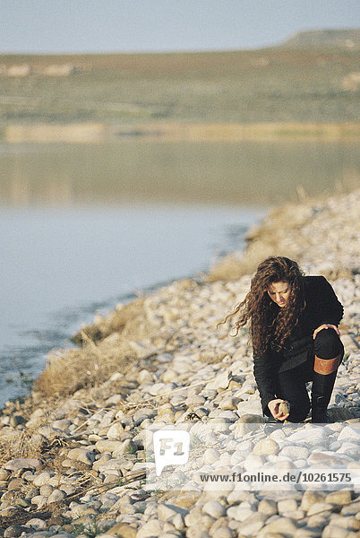 A woman collecting pebbles on the shore of a lake.