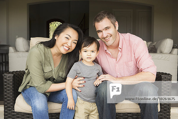 Smiling man and woman sitting side by side on a sofa  posing for a picture with their young son.