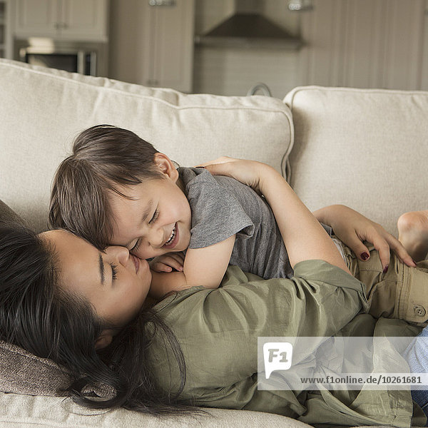 A woman lying on a sofa  smiling  cuddling her young son.