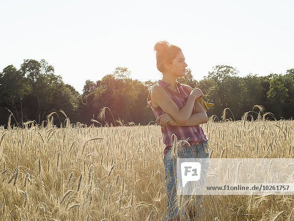 Young woman wearing a checked shirt standing in a cornfield.