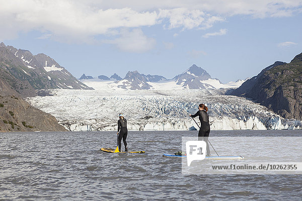Two people stand up paddleboarding in front of Grewingk Glacier  Kachemak Bay State Park  Southcentral Alaska