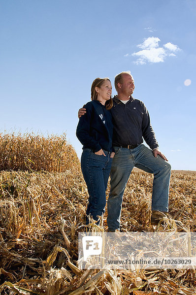 Farmer husband and wife pose together in a partially harvested grain corn field in Autumn  near Sioux City; Iowa  United States of America