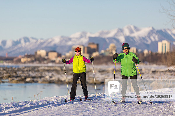 Two people cross country skiing on the Tony Knowles Coastal Trail with Anchorage in the background  Southcentral Alaska