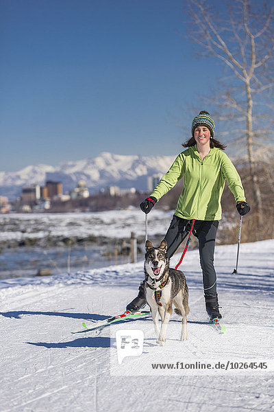 A young woman skijors with her Alaska Husky sled dog down the Tony Knowles Coastal Trail  Anchorage  Southcentral Alaska  USA.