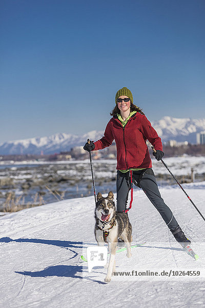 A young woman skijors with her Alaska Husky sled dog down the Tony Knowles Coastal Trail  Anchorage  Southcentral Alaska  USA.