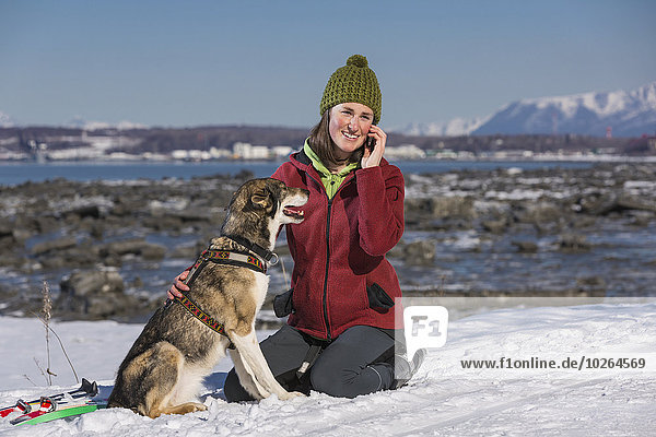 Young woman with her Alaska Husky talks on a cell phone along the Tony Knowles Coastal Trail  Anchorage  Southcentral Alaska