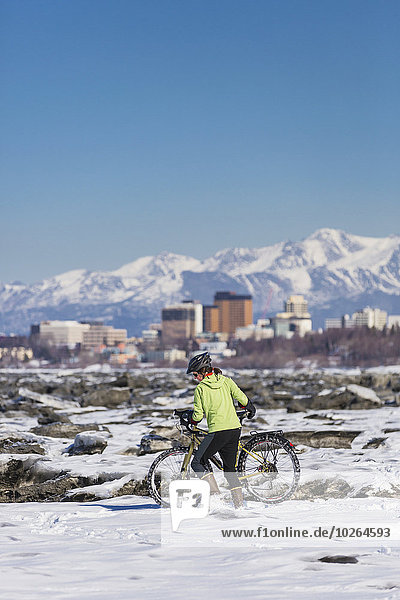 A Young Woman pushes her studded tire bicycle amongst the ice chunks in the Cook Inlet next to the Tony Knowles Coastal Trail  Anchorage  Southcentral Alaska  USA.