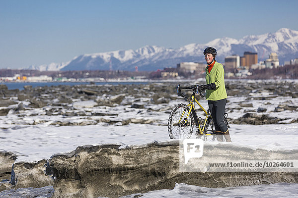 A young woman stands with her studded tire bicycle amongst the ice chunks in the Cook Inlet next to the Tony Knowles Coastal Trail  Anchorage  Southcentral Alaska  USA.
